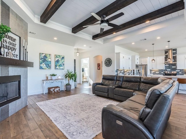 living area featuring visible vents, arched walkways, hardwood / wood-style floors, beamed ceiling, and a fireplace