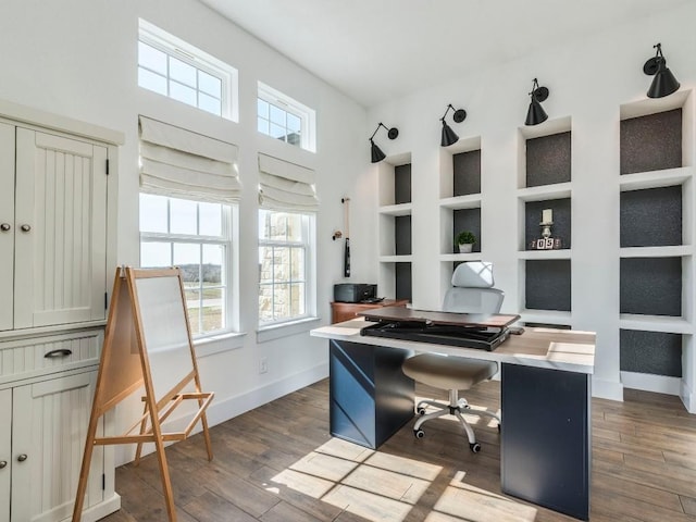 office area featuring dark wood-type flooring, built in shelves, and baseboards