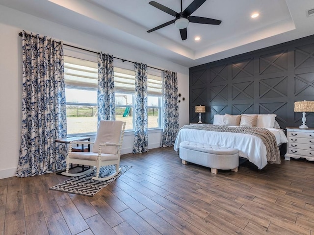 bedroom featuring visible vents, baseboards, a raised ceiling, an accent wall, and wood finished floors