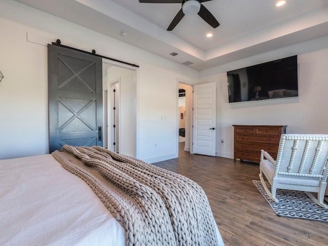 bedroom featuring a barn door, recessed lighting, wood finished floors, baseboards, and a raised ceiling