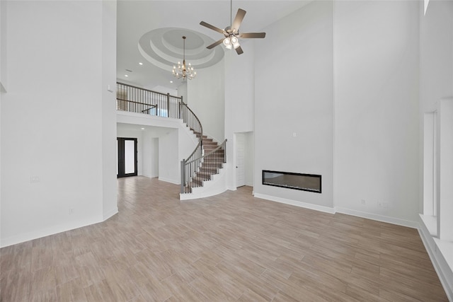 216 Echo Pass, Liberty Hill, TX 78642 - unfurnished living room with a high ceiling, stairs, a ceiling fan, light wood-style floors, and a chandelier
