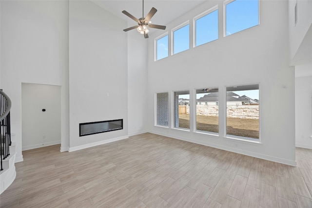 216 Echo Pass, Liberty Hill, TX 78642 - unfurnished living room with high vaulted ceiling, ceiling fan, a glass covered fireplace, light wood-type flooring, and stairs
