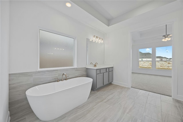216 Echo Pass, Liberty Hill, TX 78642 - bathroom with a soaking tub, vanity, tile walls, a raised ceiling, and a ceiling fan