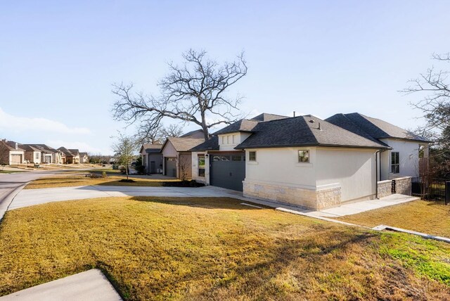 exterior space featuring a yard, stucco siding, concrete driveway, a residential view, and stone siding