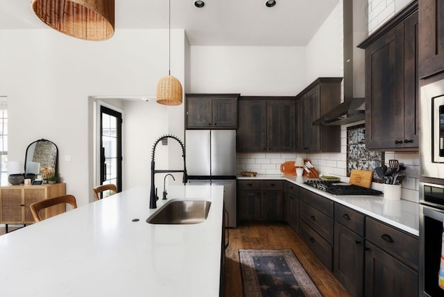 kitchen with stainless steel appliances, a sink, light countertops, wall chimney range hood, and backsplash