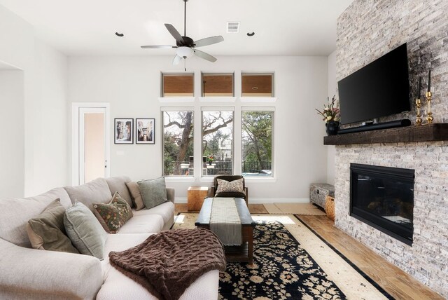 living room with baseboards, visible vents, ceiling fan, wood finished floors, and a stone fireplace