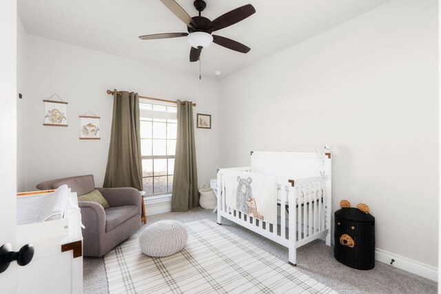 bedroom with a ceiling fan, a nursery area, carpet flooring, and baseboards