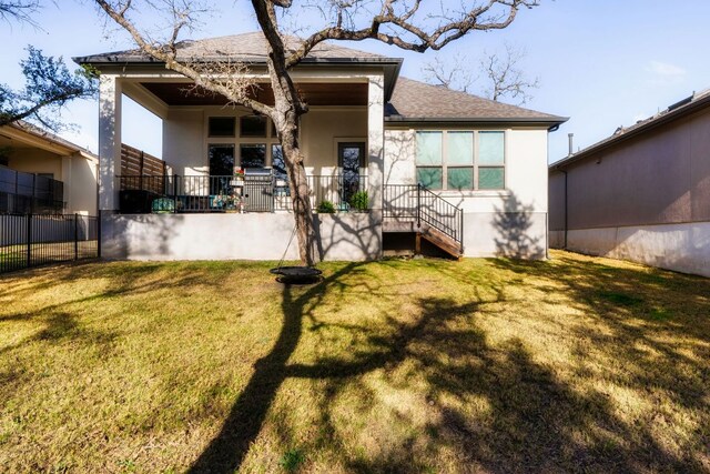 back of house with roof with shingles, a lawn, fence, and stucco siding