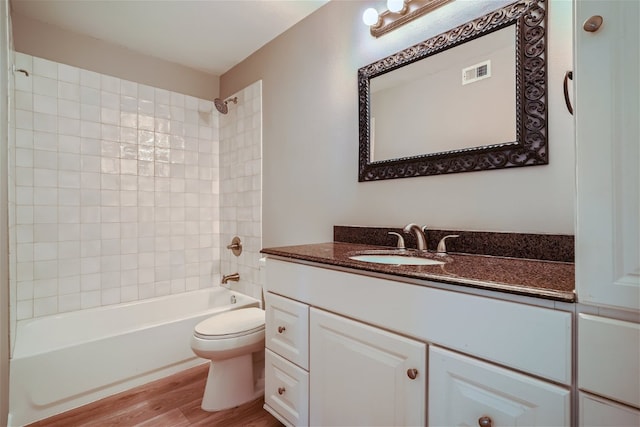 bathroom with toilet, wood finished floors, vanity, visible vents, and  shower combination