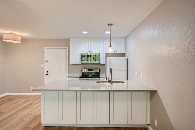 kitchen with appliances with stainless steel finishes, a peninsula, light wood-type flooring, pendant lighting, and a sink