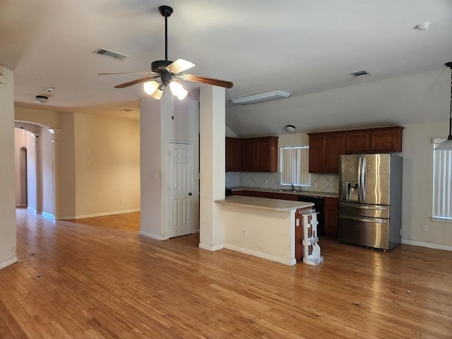 kitchen featuring arched walkways, tasteful backsplash, visible vents, light wood-style flooring, and stainless steel fridge