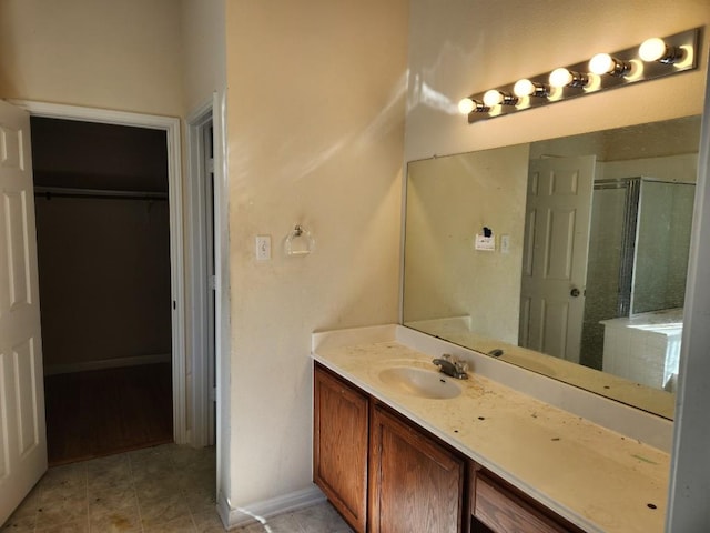 bathroom with tile patterned flooring, a shower with shower door, vanity, baseboards, and a spacious closet