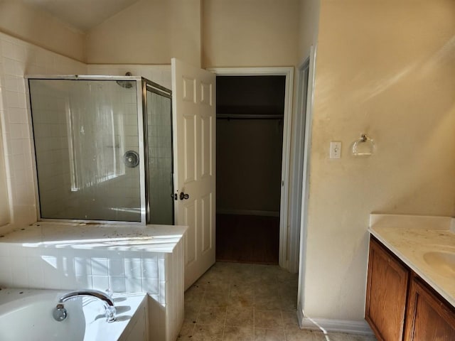 bathroom featuring a walk in closet, a garden tub, vaulted ceiling, a shower stall, and vanity