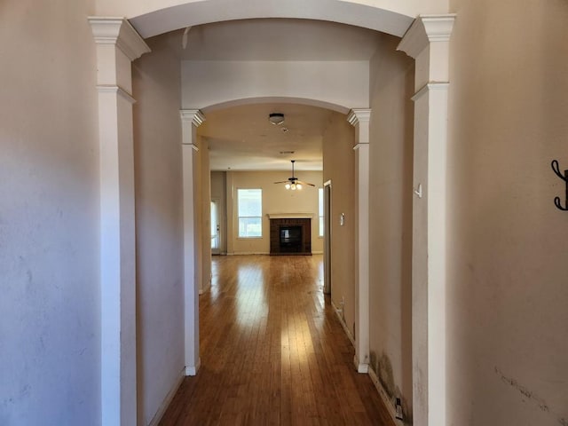 corridor with arched walkways, baseboards, hardwood / wood-style floors, and ornate columns