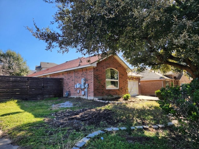 rear view of property featuring a garage, brick siding, a lawn, and fence