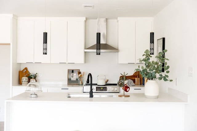 kitchen with white cabinets, light countertops, a sink, and wall chimney range hood