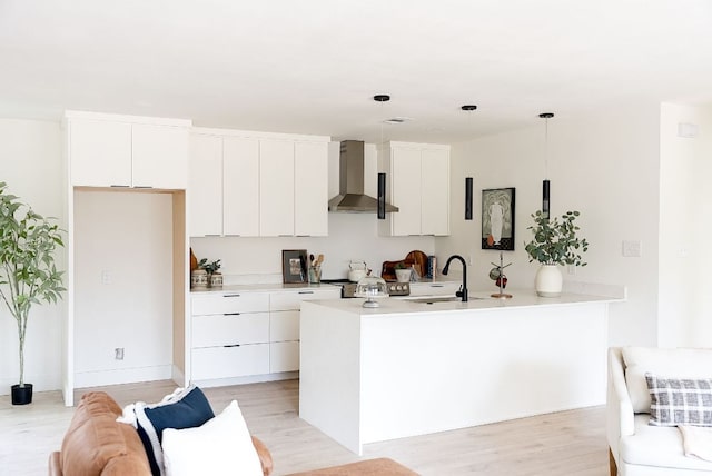 kitchen featuring wall chimney exhaust hood, a peninsula, light wood-type flooring, white cabinetry, and a sink