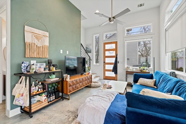 living room with concrete flooring, a towering ceiling, visible vents, a ceiling fan, and stairway