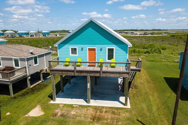 rear view of house featuring driveway, a patio area, a deck, and a lawn