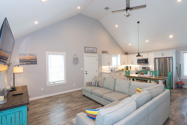 living area featuring baseboards, visible vents, a ceiling fan, dark wood-type flooring, and high vaulted ceiling