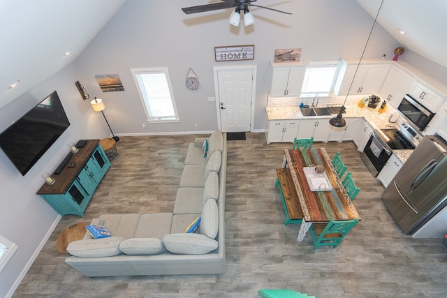 living room featuring baseboards, ceiling fan, high vaulted ceiling, and wood finished floors