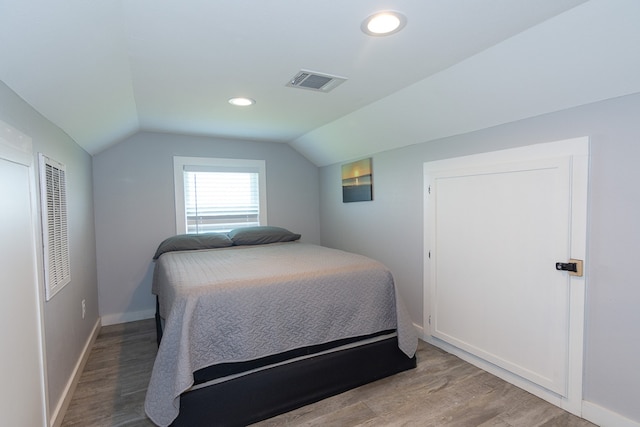 bedroom featuring light wood finished floors, baseboards, visible vents, and vaulted ceiling