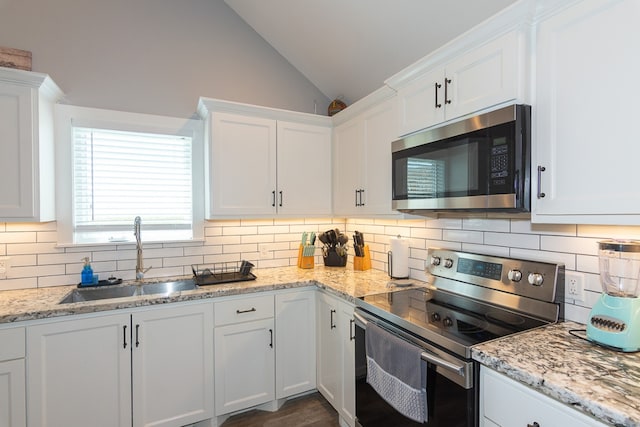 kitchen with vaulted ceiling, appliances with stainless steel finishes, a sink, and white cabinetry