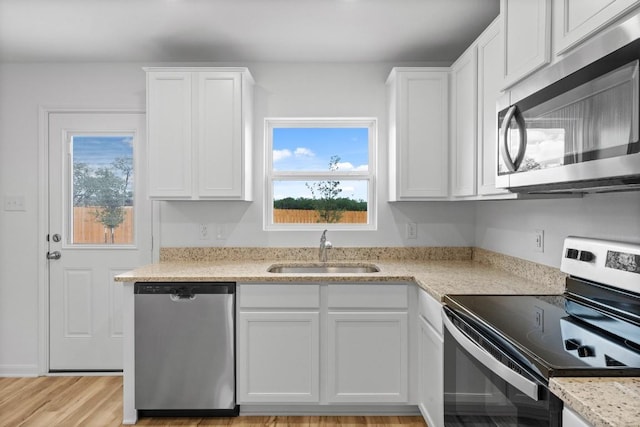 kitchen featuring stainless steel appliances, light wood-style floors, white cabinets, a sink, and light stone countertops