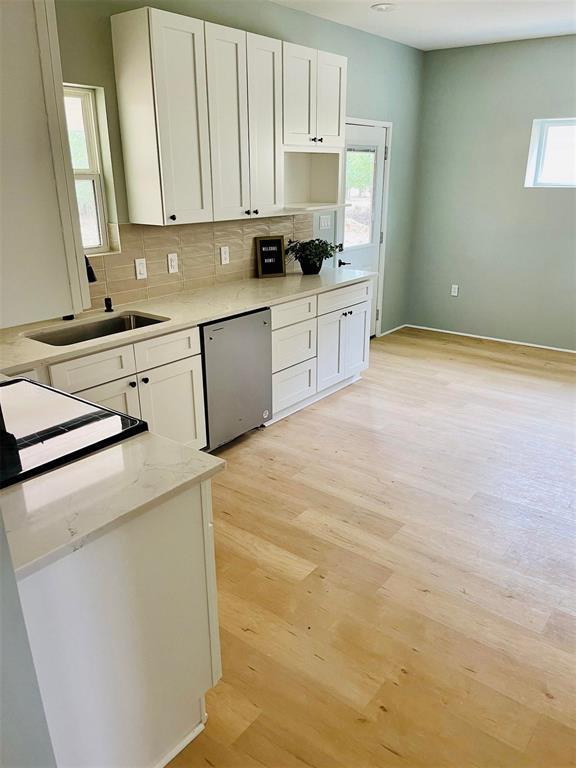 kitchen with dishwasher, backsplash, light wood-style floors, white cabinetry, and a sink