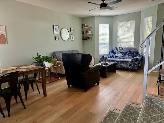 living area featuring ceiling fan, light wood finished floors, and stairs