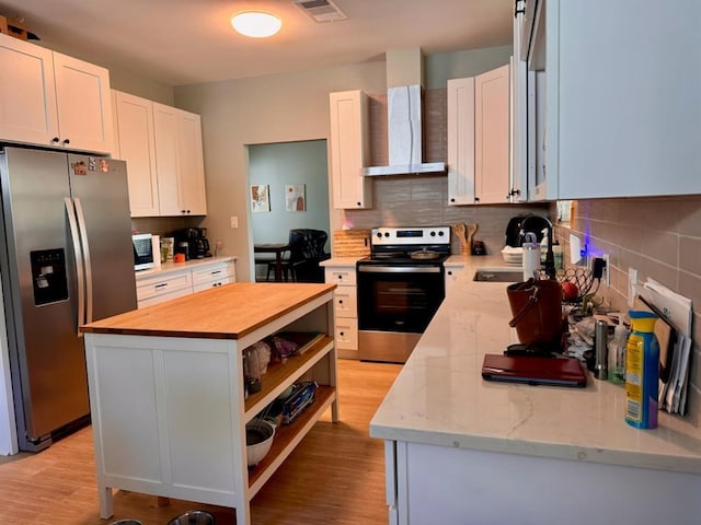 kitchen featuring visible vents, wall chimney exhaust hood, a kitchen island, butcher block countertops, and appliances with stainless steel finishes