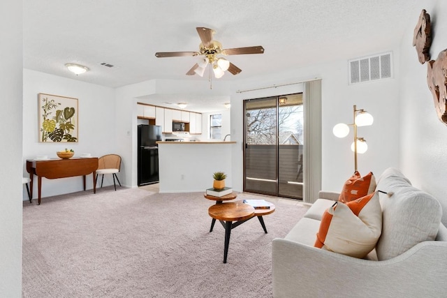 living area featuring light carpet, ceiling fan, a textured ceiling, and visible vents