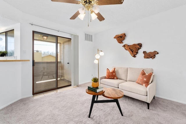 carpeted living area with baseboards, a textured ceiling, visible vents, and a ceiling fan