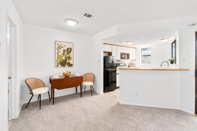 kitchen featuring visible vents, stainless steel microwave, freestanding refrigerator, light carpet, and a textured ceiling