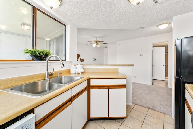 kitchen with light countertops, freestanding refrigerator, white cabinets, a sink, and light tile patterned flooring