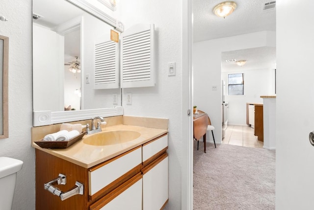 bathroom featuring visible vents, toilet, ceiling fan, vanity, and a textured ceiling