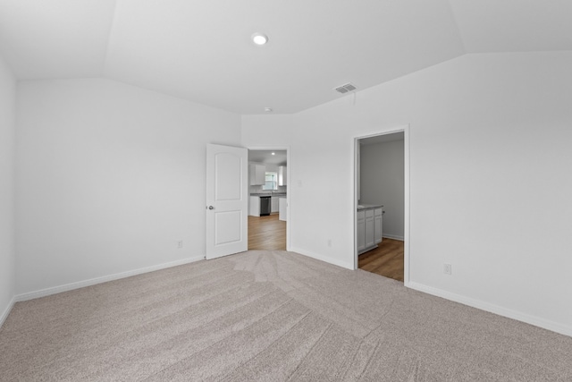 unfurnished bedroom with ensuite bathroom, visible vents, baseboards, vaulted ceiling, and carpet