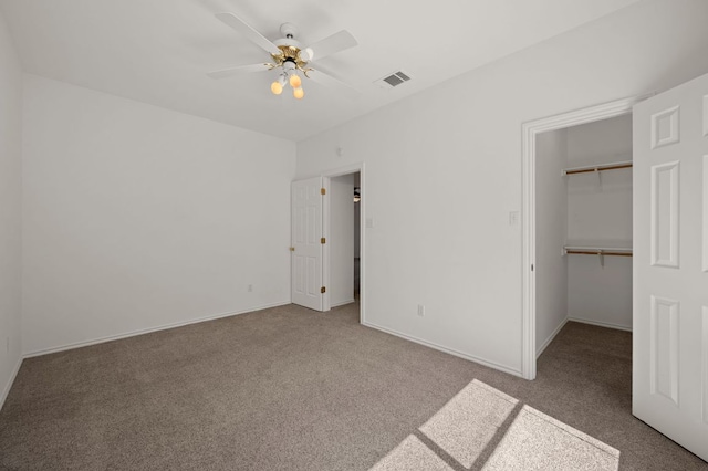 unfurnished bedroom featuring a walk in closet, visible vents, ceiling fan, and carpet