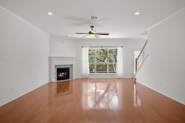 unfurnished living room featuring wood finished floors, visible vents, a high end fireplace, stairs, and crown molding