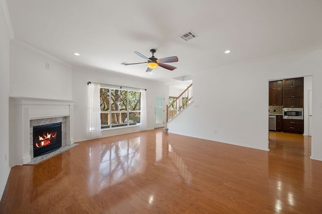 unfurnished living room with a high end fireplace, visible vents, light wood-style floors, stairway, and crown molding