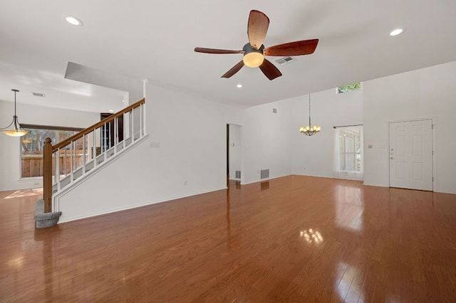 unfurnished living room featuring recessed lighting, visible vents, stairway, wood finished floors, and ceiling fan with notable chandelier