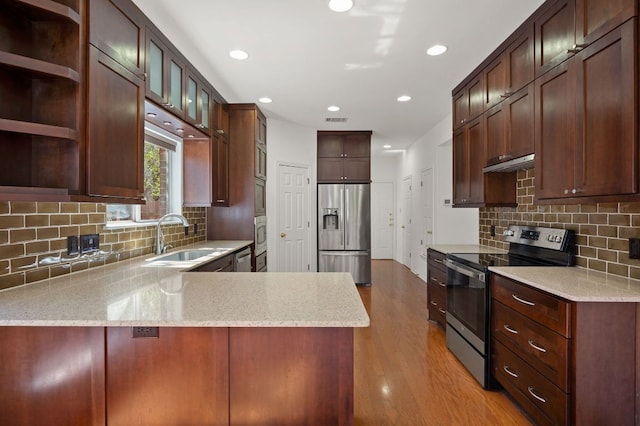 kitchen with light wood-style floors, a peninsula, stainless steel appliances, under cabinet range hood, and a sink