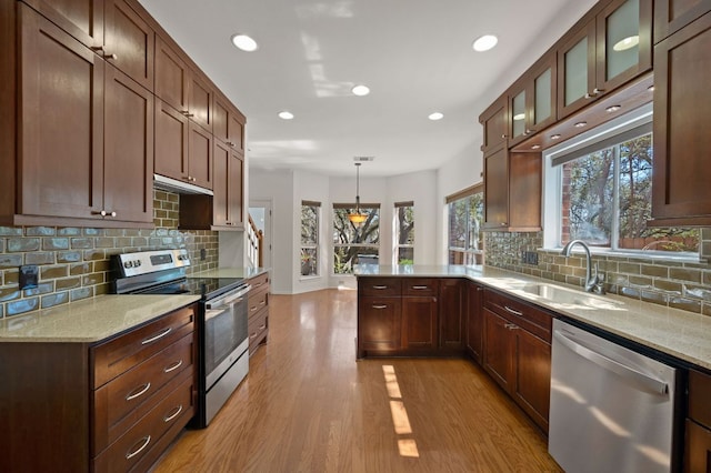 kitchen with a peninsula, light stone countertops, stainless steel appliances, light wood-style floors, and a sink