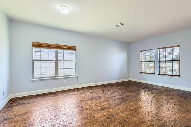 spare room with dark wood-style flooring, visible vents, and baseboards