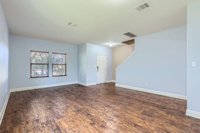 empty room with stairs, dark wood finished floors, visible vents, and baseboards