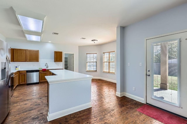 kitchen with stainless steel appliances, visible vents, brown cabinets, dark wood-style floors, and tasteful backsplash