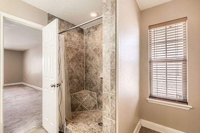 bathroom with a tile shower and baseboards