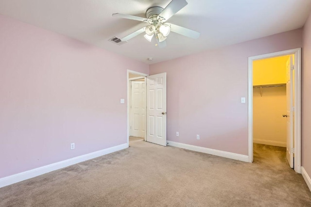 unfurnished bedroom with light carpet, baseboards, visible vents, a ceiling fan, and a walk in closet