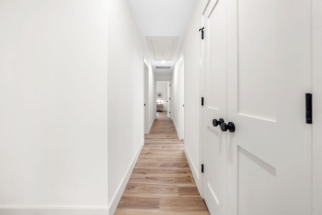 hallway with light wood finished floors, attic access, and baseboards