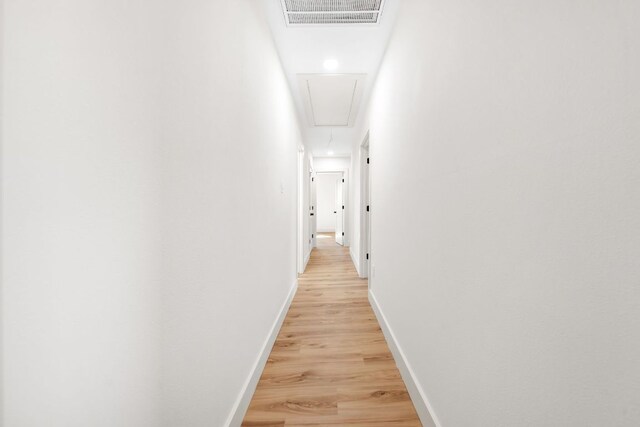 hallway featuring light wood-style floors, attic access, visible vents, and baseboards